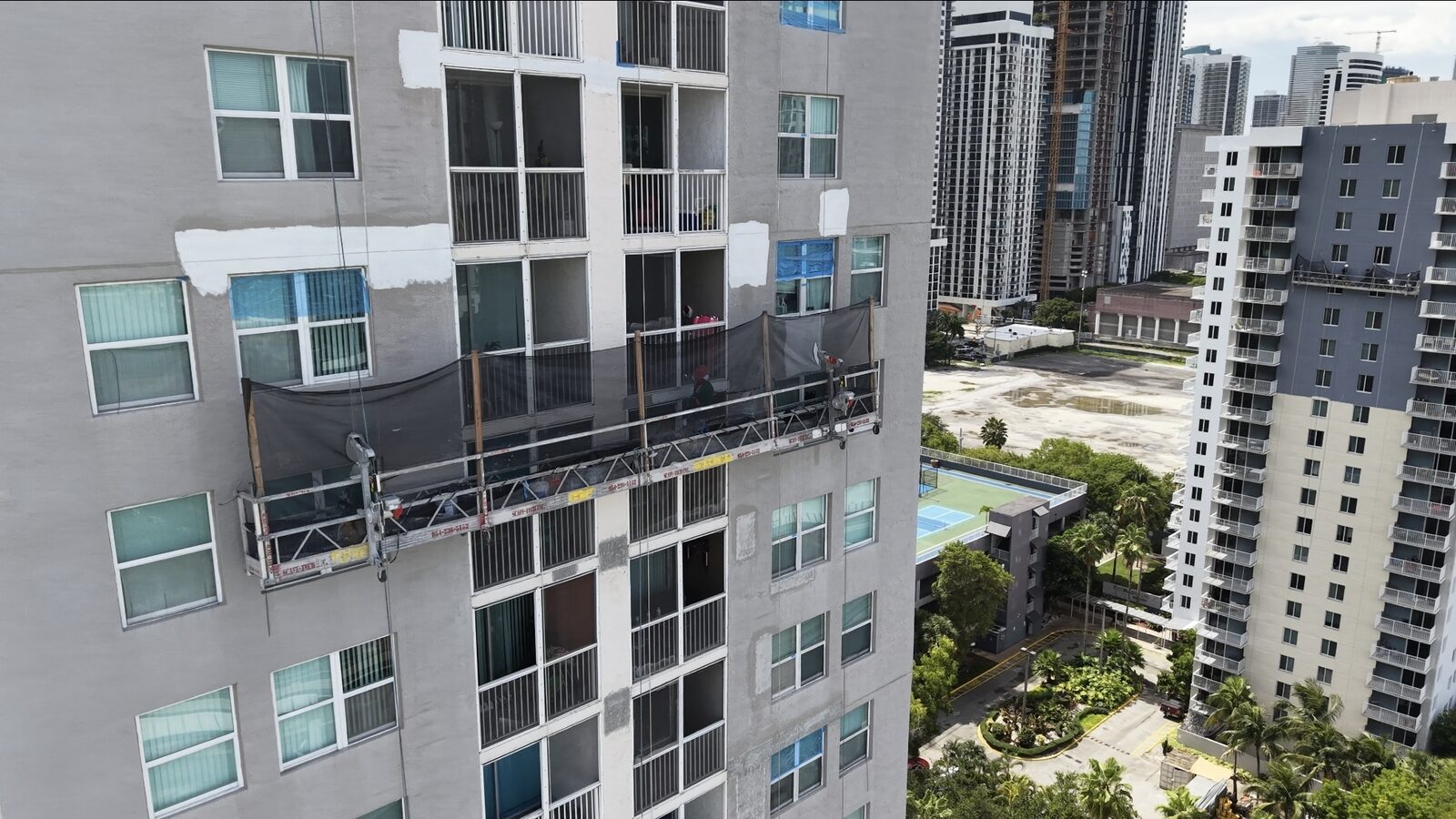 A Park Place by the Bay facade mid-restoration — swing stage and freshly patched stucco during the program